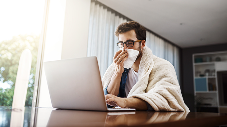 Homem com o lenço no nariz de frente para o computador