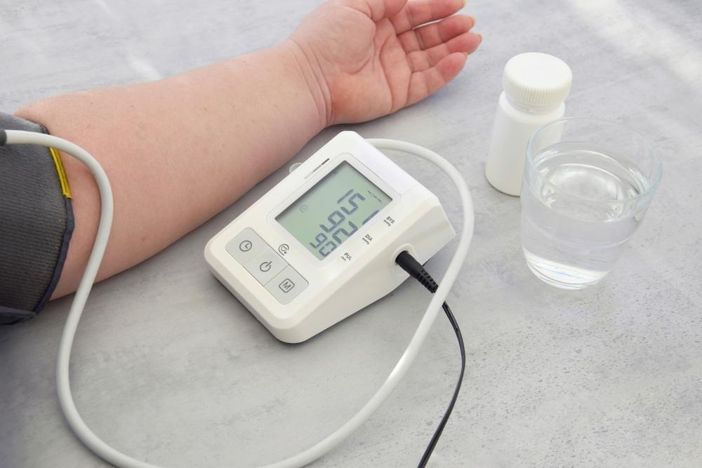 Pessoa medindo a pressão arterial com aparelho digital, representando controle da hipertensão em idosos, uso de medicação e prevenção de AVC.